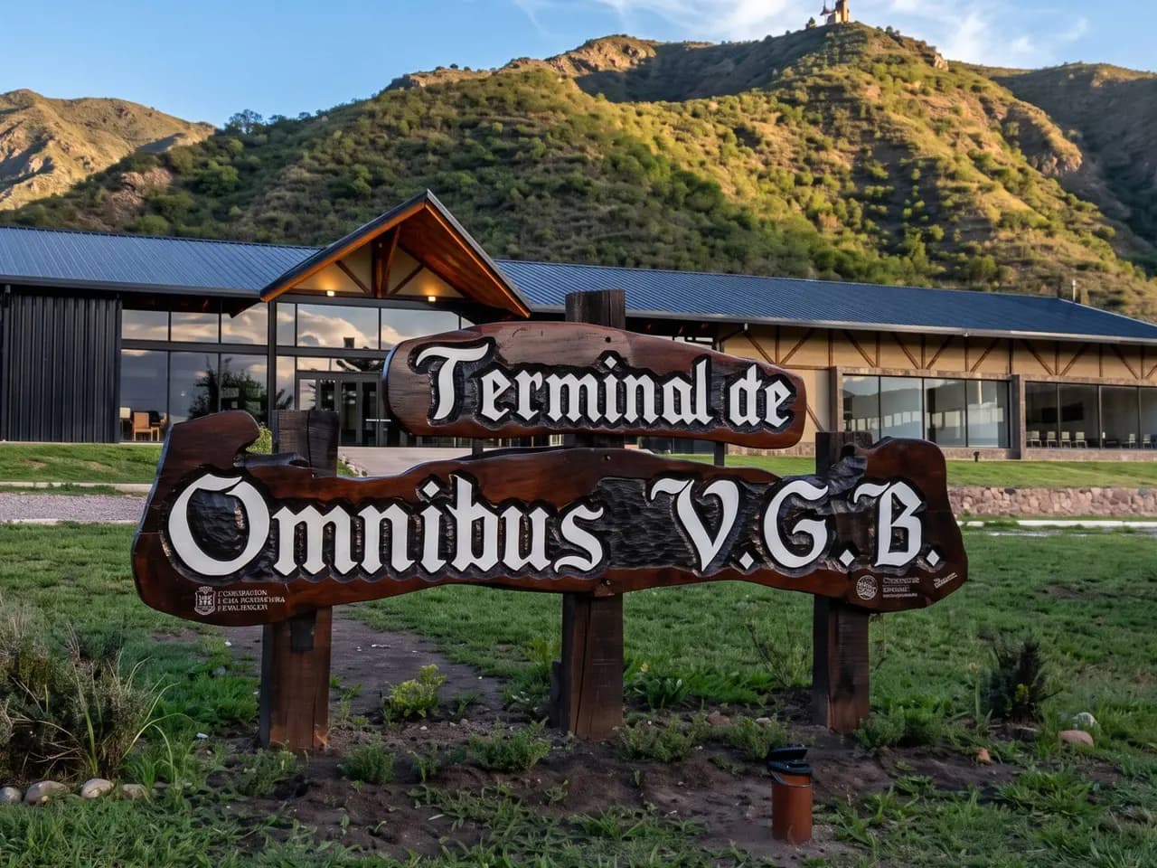 Cartel de madera tallada de la terminal de ómnibus de Villa General Belgrano, con las sierras detrás