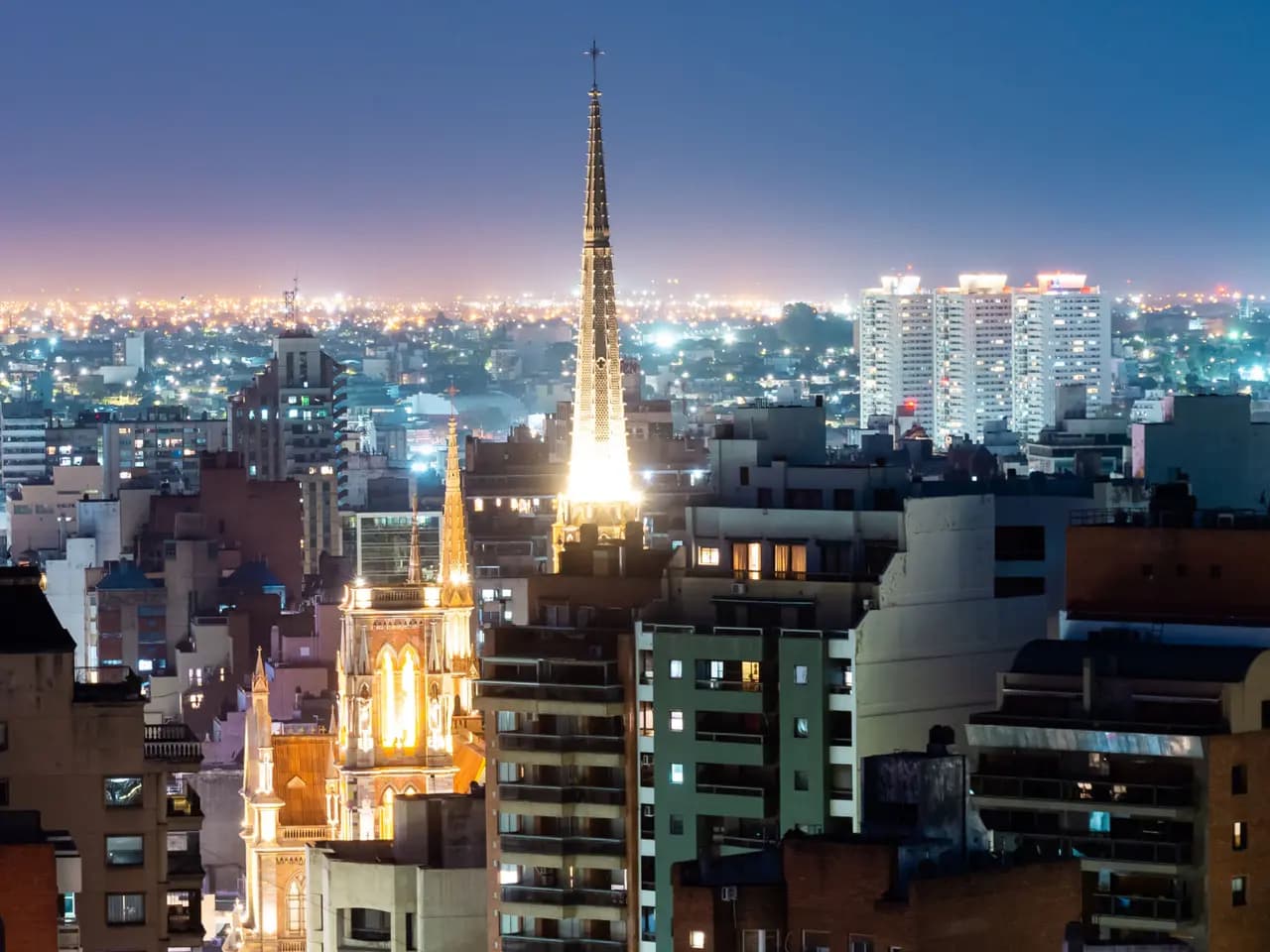 La ciudad de Córdoba de noche, con la torre iluminada de una iglesia sobre los edificios