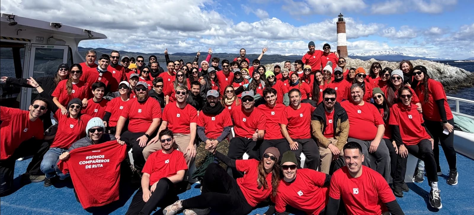 El equipo de Plataforma10 con remeras rojas de la marca en un barco por el Canal Beagle, frente al faro Les Éclaireurs, en Ushuaia
