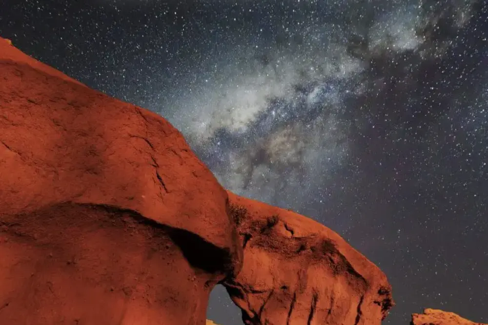 La Vía Láctea sobre una formación de roca rojiza iluminada, en un cielo cubierto de estrellas