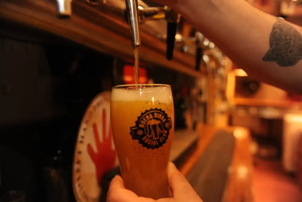 Un vaso con el logo de una cervecería se llena de cerveza dorada bajo una canilla, frente a la barra