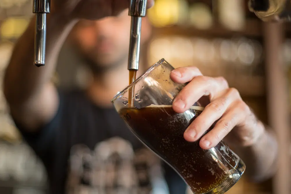 Un bartender sirve cerveza negra de la canilla en un vaso inclinado