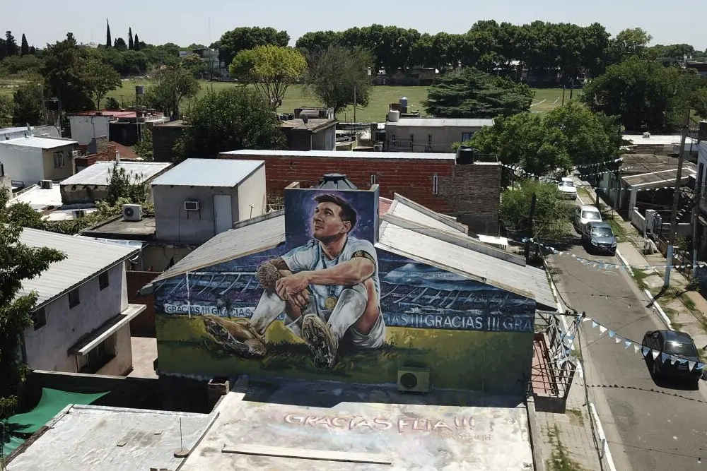 Mural de Messi sentado en el césped con la medalla, pintado sobre una casa de un barrio de casas bajas, con la palabra “Gracias” repetida
