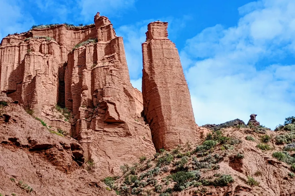 Paredones y torres de roca rojiza con capas horizontales, bajo un cielo azul con nubes