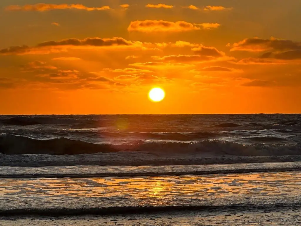 Sol naranja saliendo sobre el mar, con el cielo encendido y el reflejo dorado en la orilla mojada
