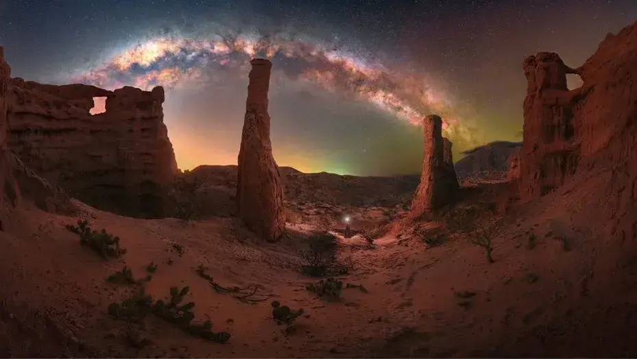 La Vía Láctea en arco sobre formaciones de roca roja con forma de columnas, de noche