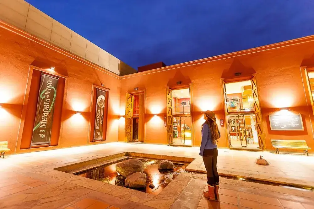 Una mujer con sombrero en el patio iluminado del Museo de la Vid y el Vino, al anochecer