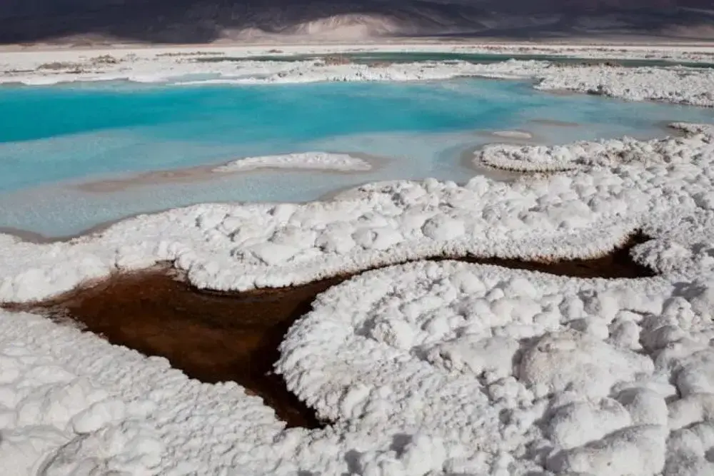 Costra de sal blanca alrededor de pozones de agua turquesa y rojiza en un salar
