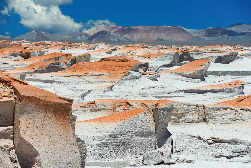 Formaciones de piedra pómez blancas con cumbres anaranjadas, y cerros de la Puna al fondo
