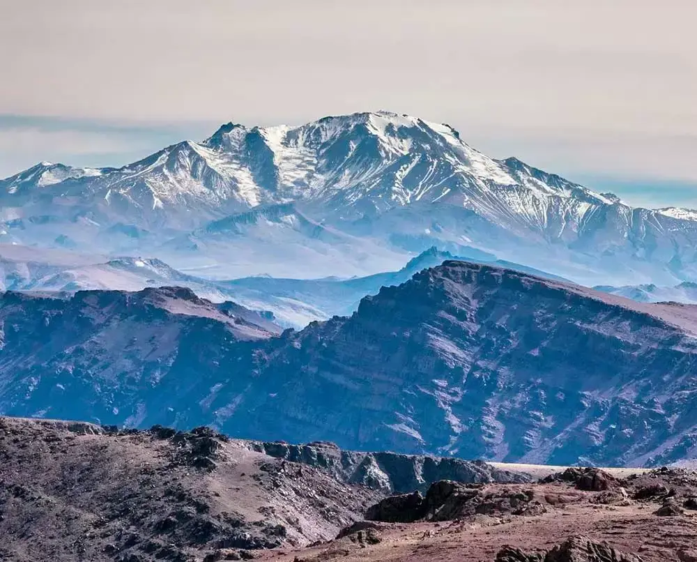 Cumbre nevada de una montaña muy alta que se eleva detrás de cordones oscuros y áridos
