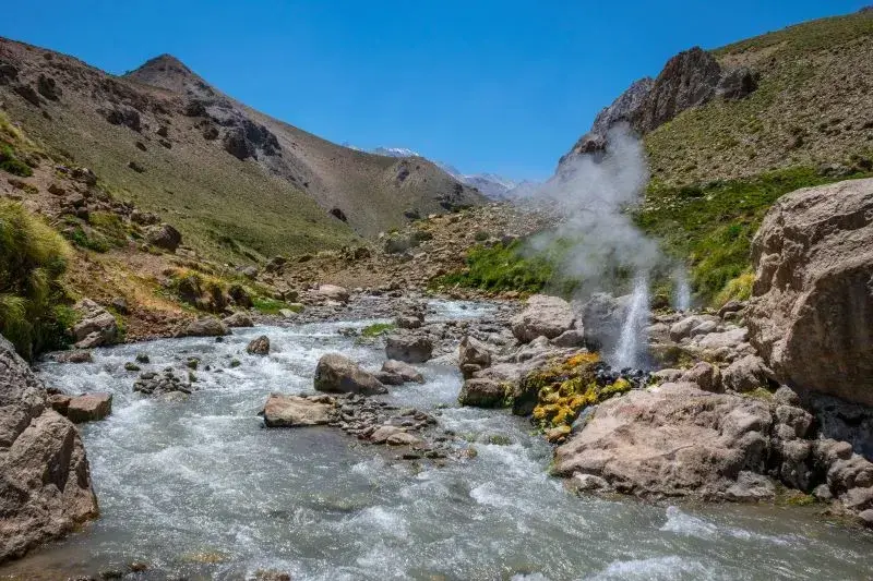 Arroyo de montaña entre rocas con un chorro de agua termal y vapor que sube junto a la orilla