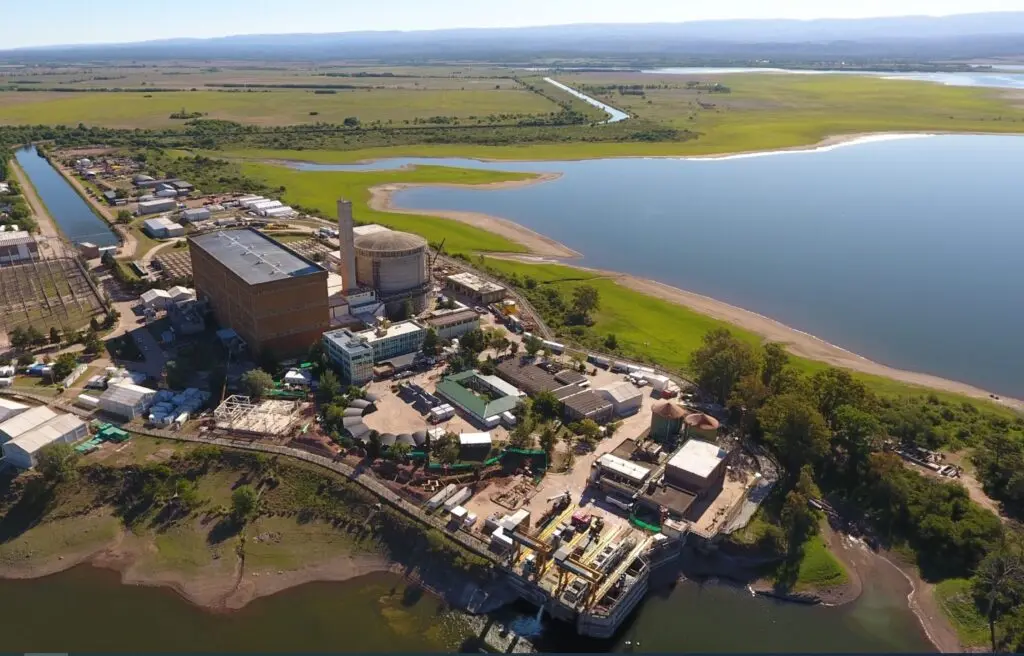 Vista aérea de la Central Nuclear Embalse, con su cúpula y edificios industriales a orillas del lago y el campo de fondo