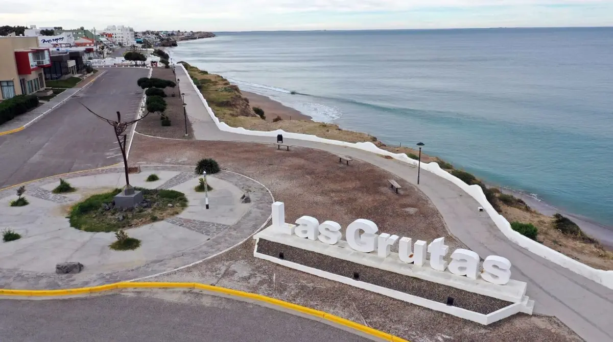 Letras blancas con el nombre del balneario sobre la costanera, con el paseo y el mar calmo al costado