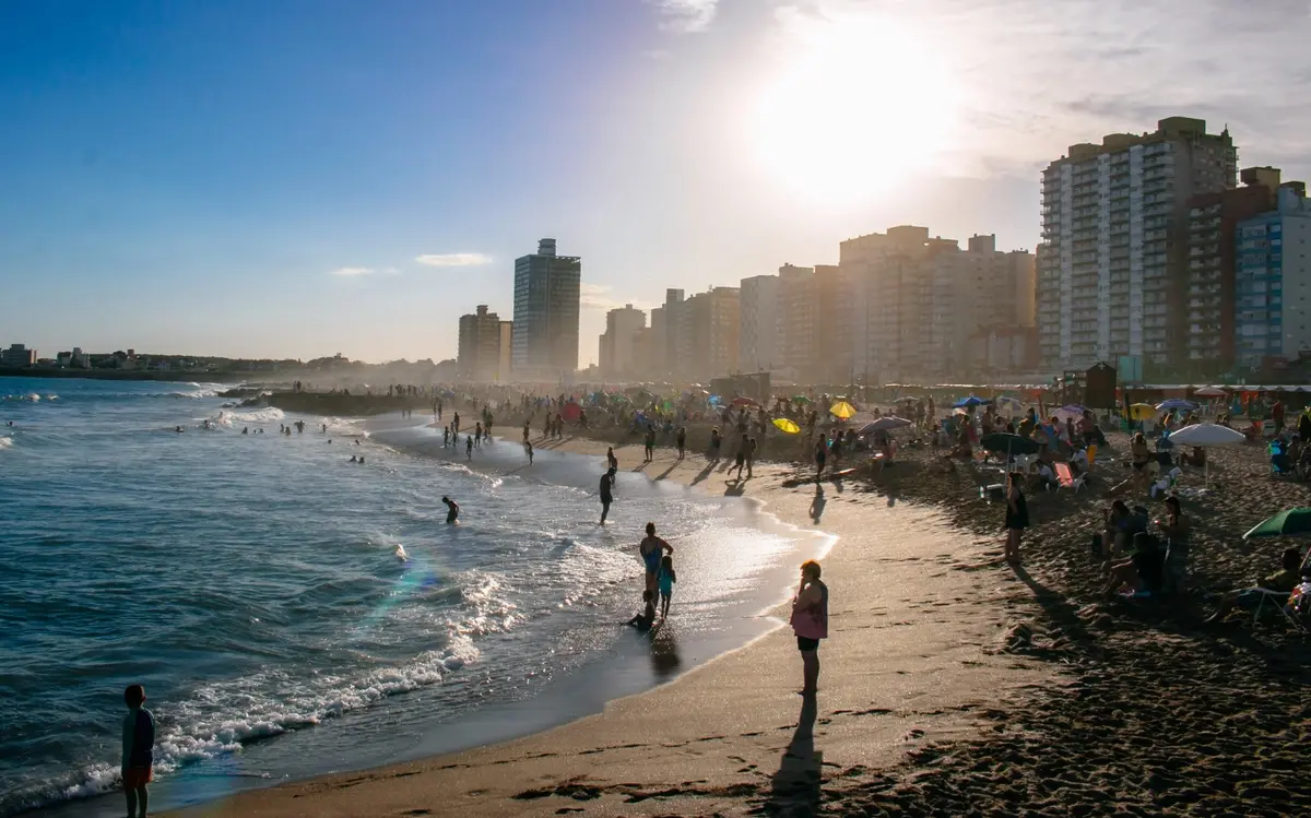 Playa de Miramar al atardecer, con gente en la orilla, sombrillas y una hilera de edificios a contraluz