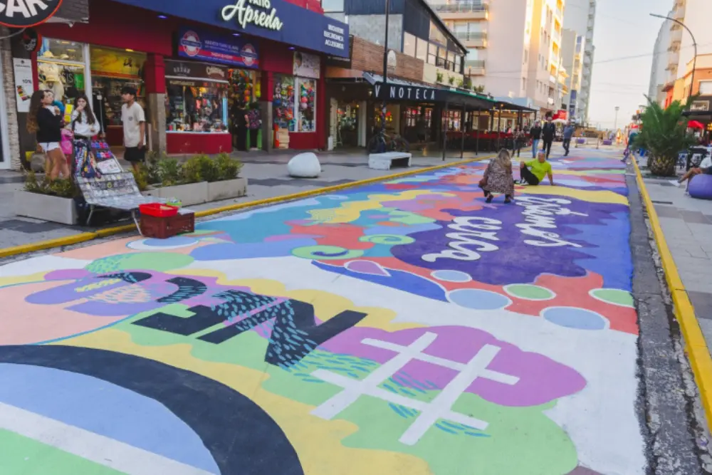 Calle peatonal con el asfalto pintado con dibujos de colores, locales comerciales a los costados y gente caminando
