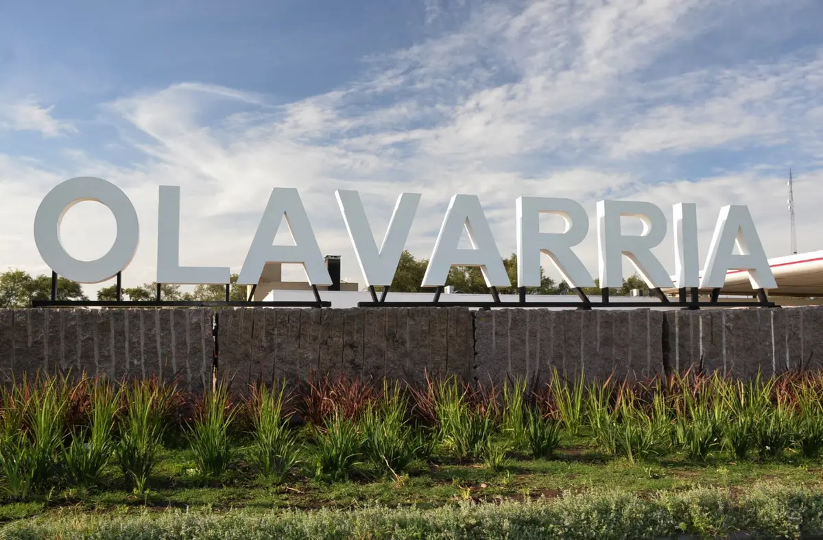 Letras blancas gigantes que forman la palabra Olavarria sobre un muro de piedra, con plantas al pie y cielo celeste