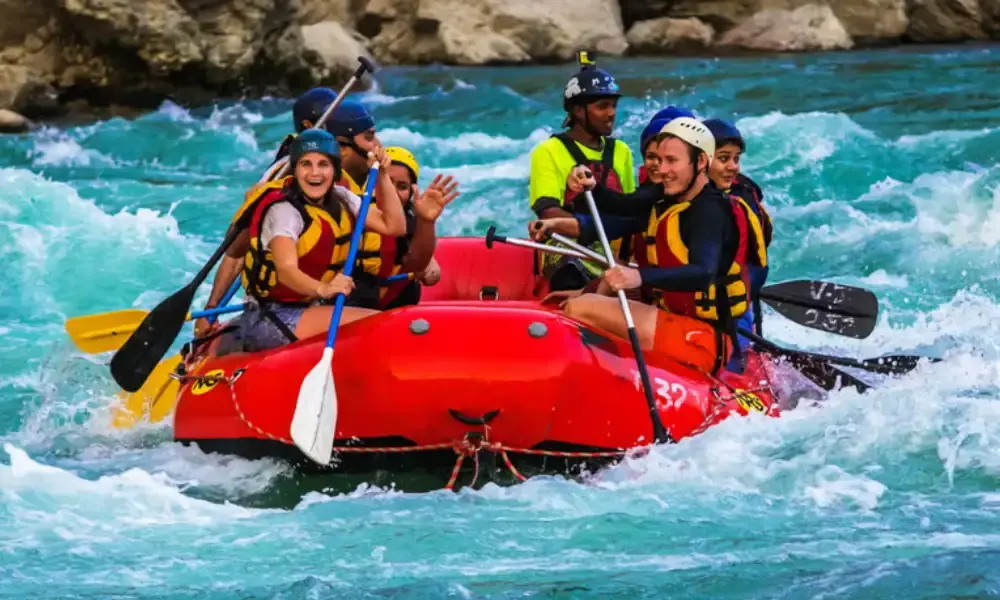 Grupo con cascos y chalecos salvavidas remando en un gomón rojo entre olas de agua turquesa