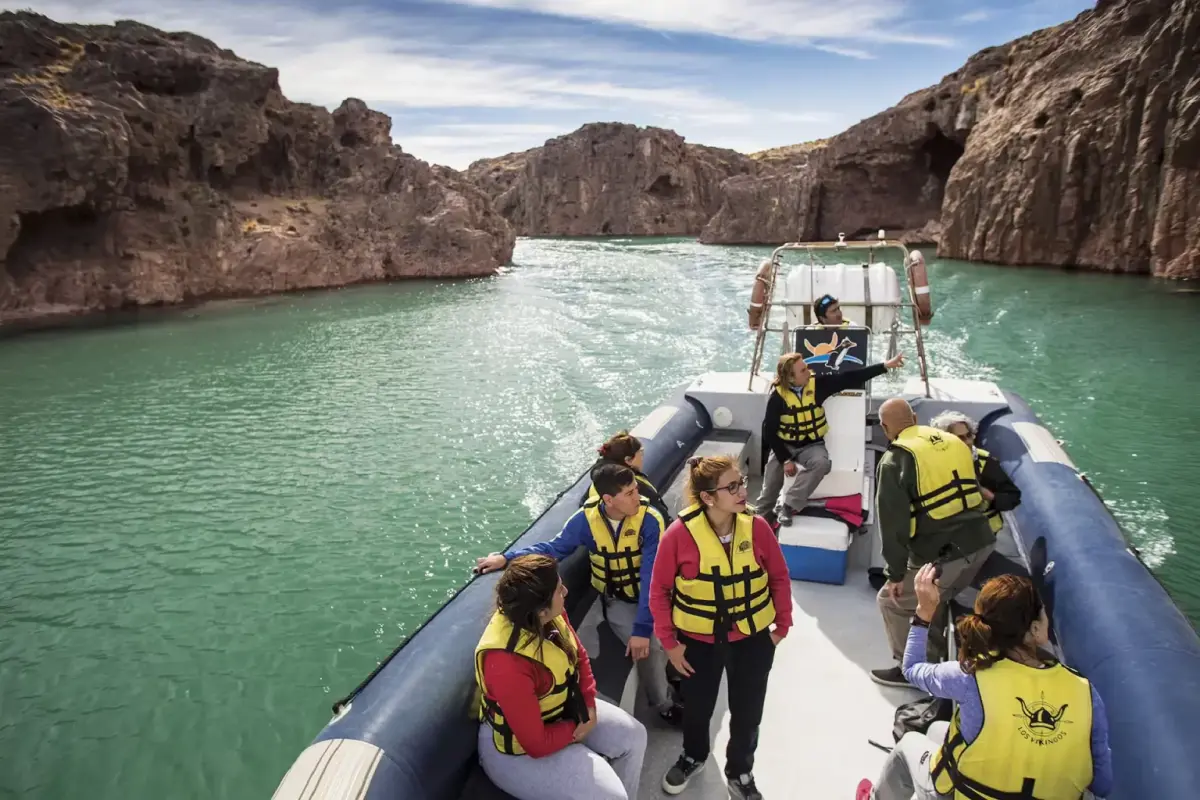 Un grupo de turistas con chalecos salvavidas navega en un gomón por un cañadón de paredes rojizas sobre agua verde
