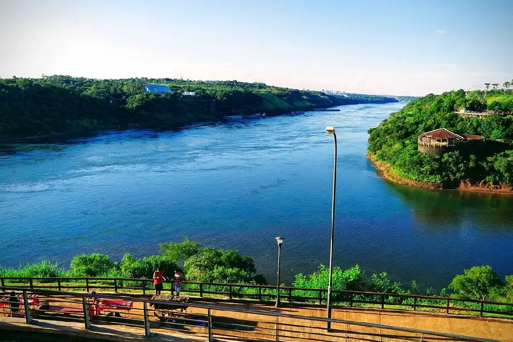Vista desde el mirador del Hito Tres Fronteras: el río ancho entre costas de selva, con una baranda y gente mirando el paisaje