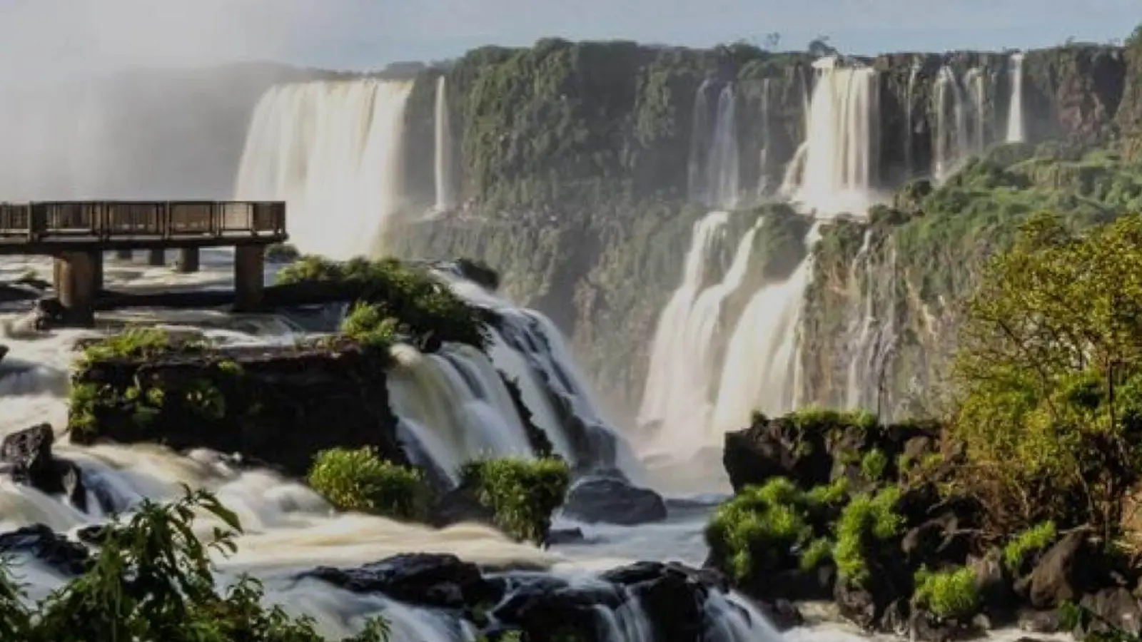 Saltos de las Cataratas del Iguazú cayendo entre la selva, con una pasarela que avanza sobre el agua y una nube de vapor
