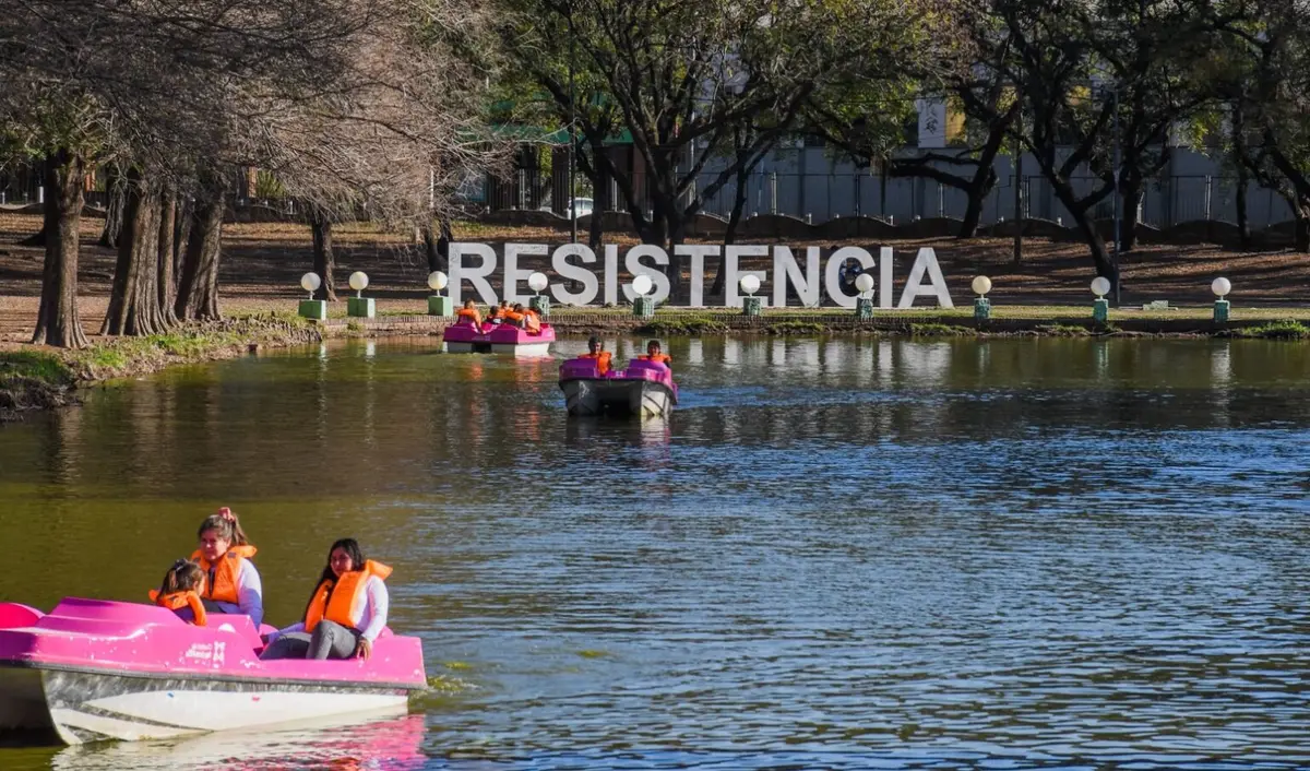 Botes a pedal con chicos y chalecos naranjas en una laguna, con las letras gigantes de Resistencia en la orilla