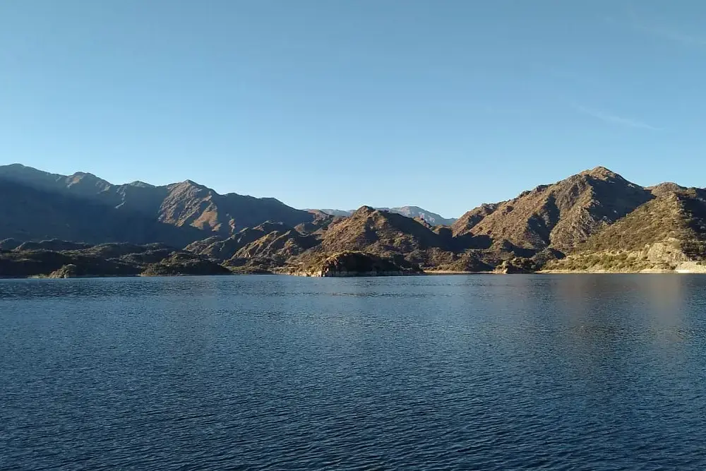 Un embalse de aguas azules y quietas rodeado de cerros áridos bajo un cielo despejado