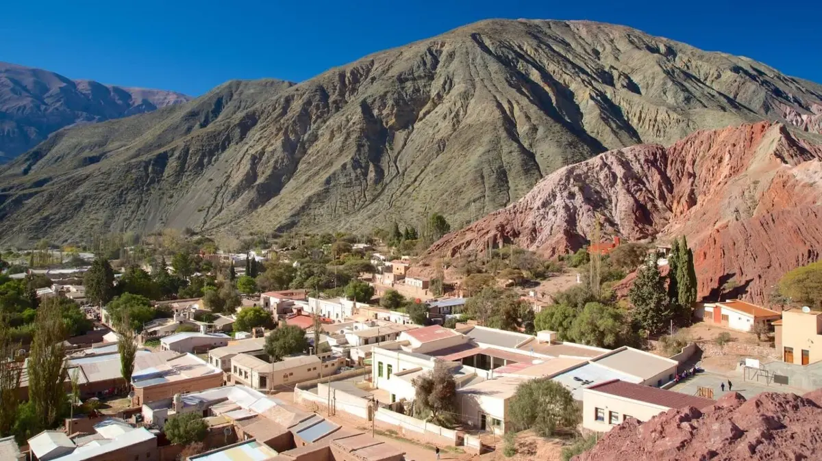 Vista desde lo alto del pueblo de Purmamarca, con casas bajas, árboles y cerros rojizos y verdes detrás