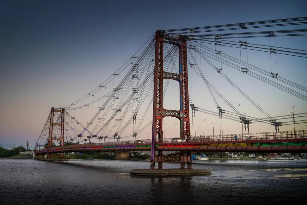 El Puente Colgante de Santa Fe, de estructura roja con sus cables tensores, sobre la laguna al anochecer