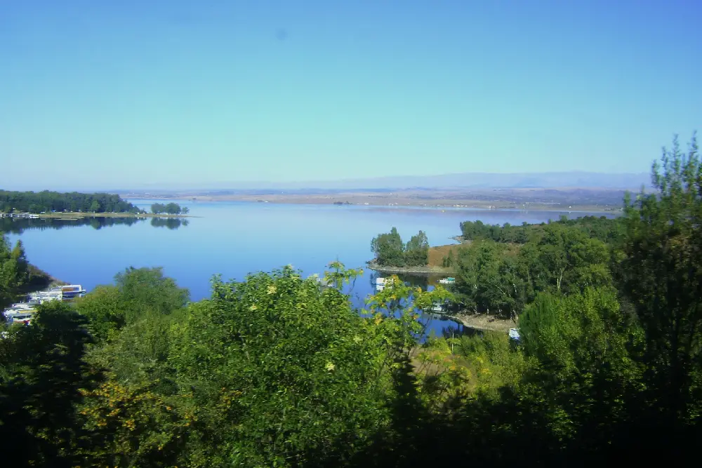 El lago del Dique Los Molinos visto desde un mirador entre árboles, con lanchas amarradas en la orilla