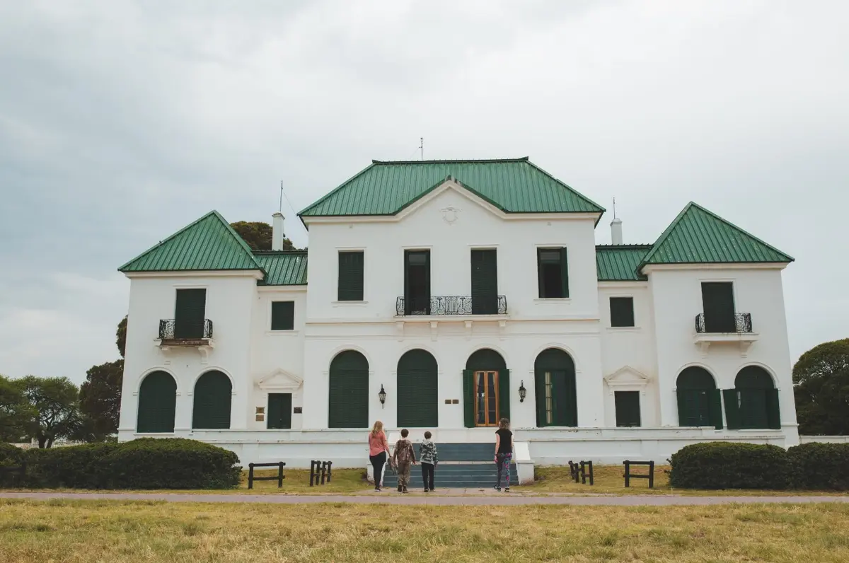 Casona blanca de estilo francés con techos verdes y ventanas en arco, con una familia caminando hacia la entrada