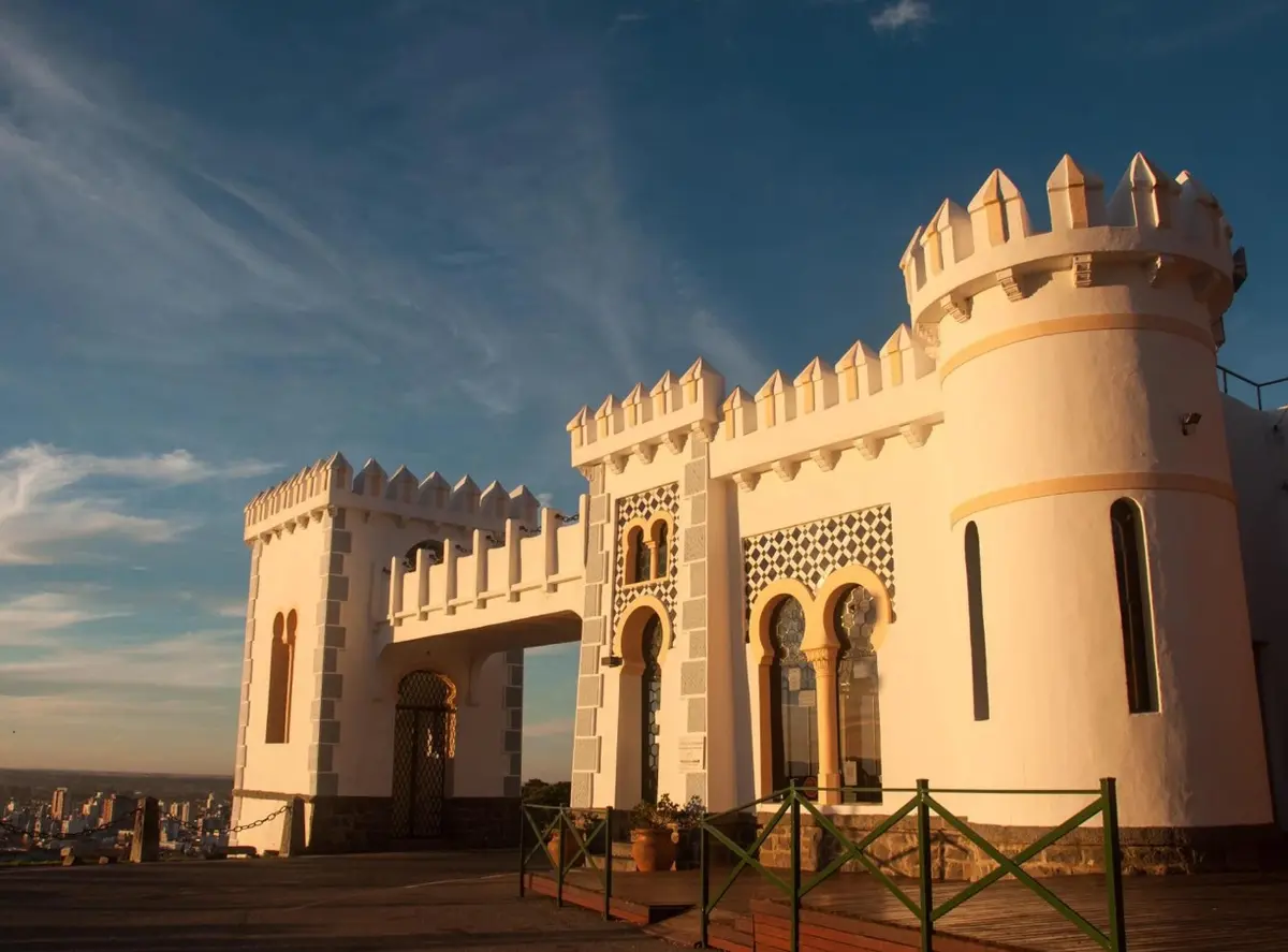 El Castillo Morisco, blanco y con almenas, iluminado por el sol del atardecer, con la ciudad abajo a la izquierda