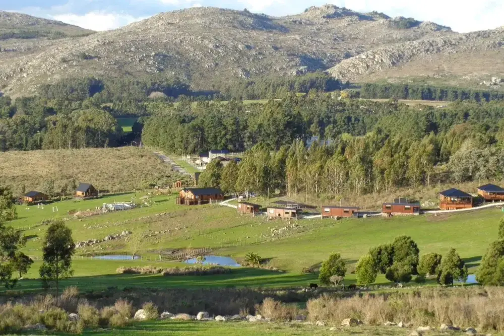 Valle verde con cabañas y lagunitas, bosques de pinos y eucaliptos y las sierras rocosas de Tandil detrás