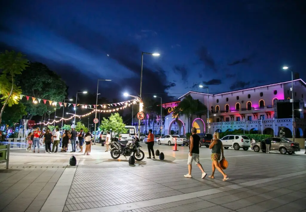 Edificio de estilo colonial con arcos iluminados de noche y gente paseando por la vereda de enfrente