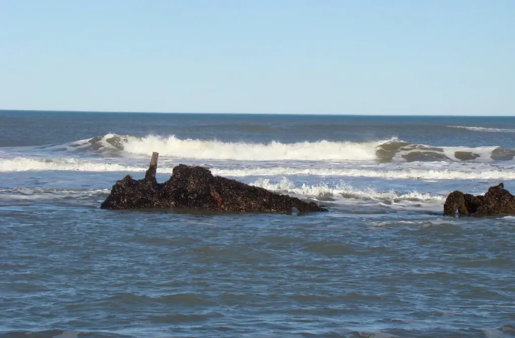 Olas rompiendo en la orilla del mar alrededor de unas rocas oscuras que asoman del agua