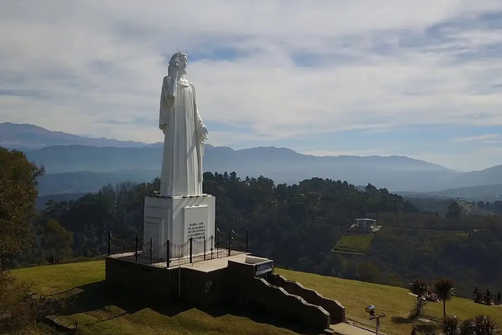 La estatua blanca del Cristo Bendicente sobre su pedestal en el cerro San Javier, con cerros boscosos y montañas detrás