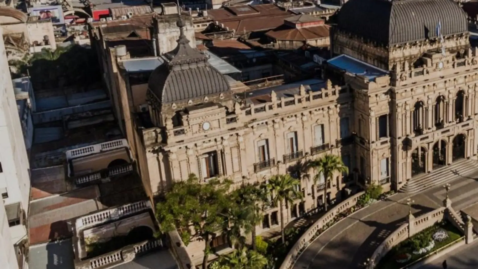 Vista aérea de la Casa de Gobierno de Tucumán, con sus cúpulas oscuras, la escalinata y palmeras frente a la fachada