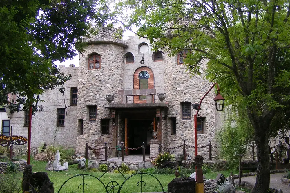 Fachada del Castillo Romano, un edificio de piedra con torres redondas y ventanas en arco, rodeado de jardín