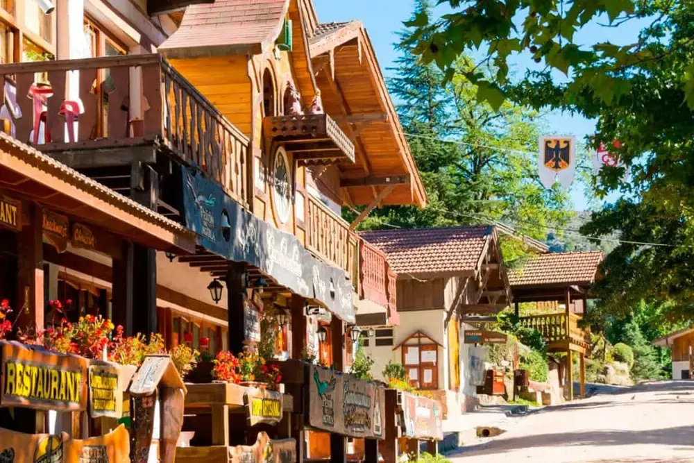 Calle del centro de Villa General Belgrano con casas de madera de estilo alpino, carteles de restaurantes y flores