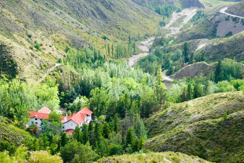 El hotel de techos rojos entre álamos y pinos, en el fondo de un valle verde atravesado por un camino de montaña