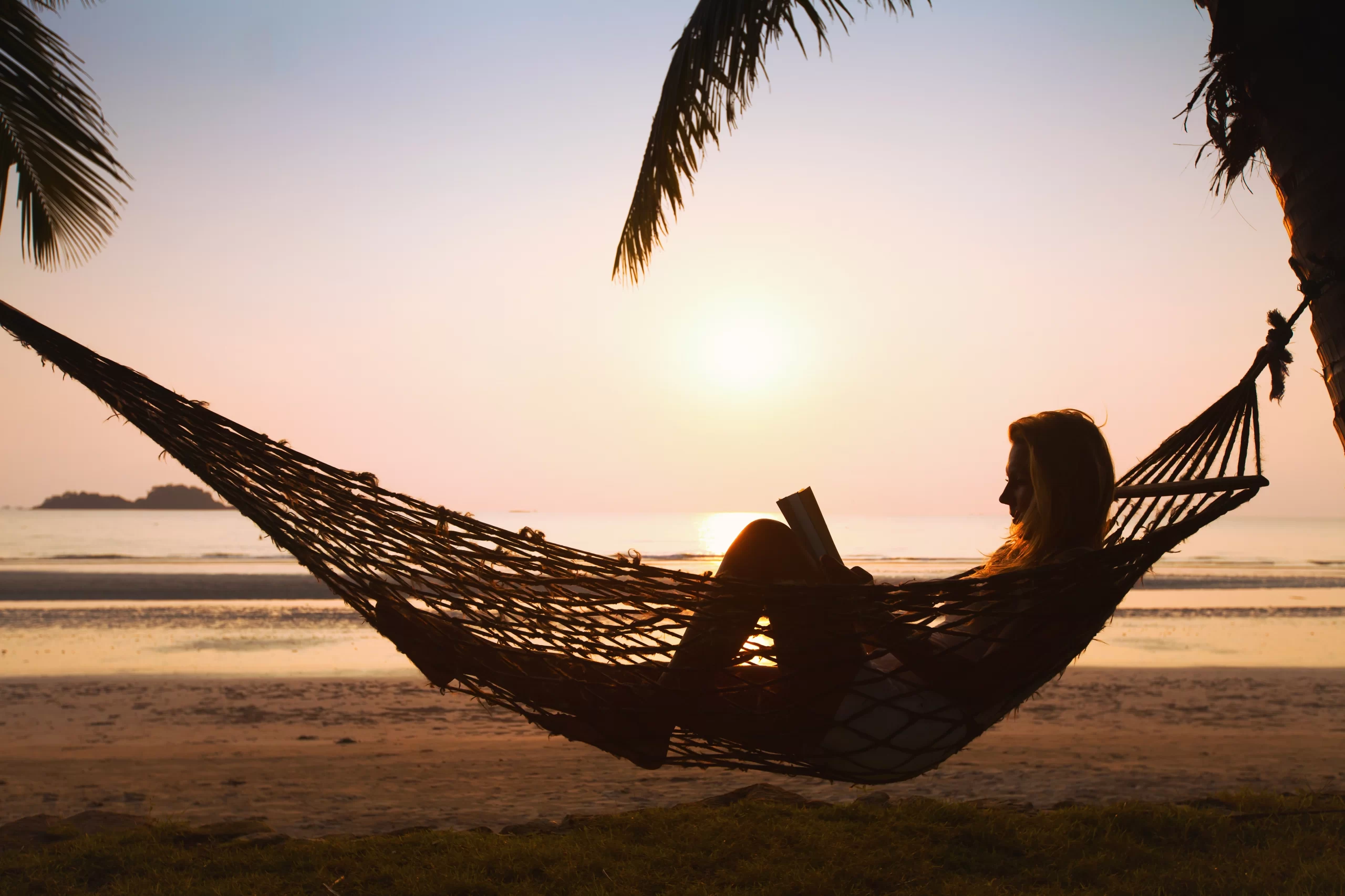Mujer leyendo un libro en una hamaca durante la puesta de sol.