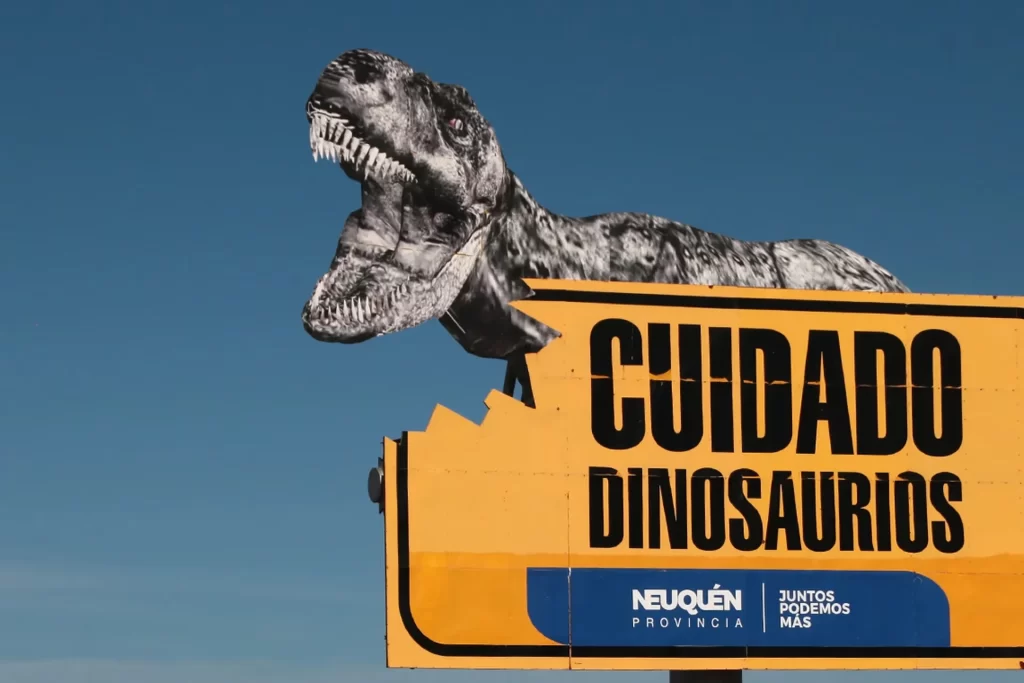 Cartel de entrada a el Chocón con un dinosaurio mordiendo el cartel
