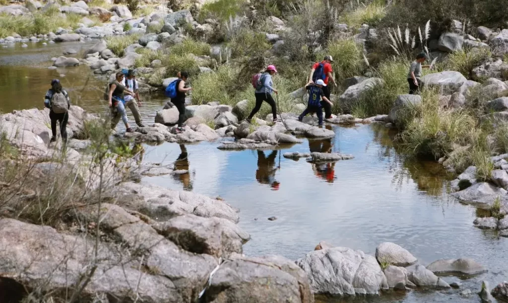 Personas cruzando un arroyo mientras hacen trekking en la sierra
