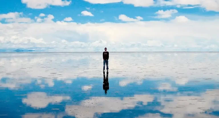 Hombre parado sobre el Salar de Uyuni donde se refleja el cielo sobre el suelo
